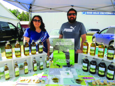 two people standing in farmers market tent behind product display