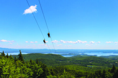 2 people high on a zipline over green forests and blue sky
