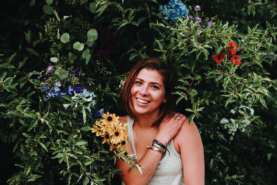 woman in tank top outdoors, posing with flowering bushes