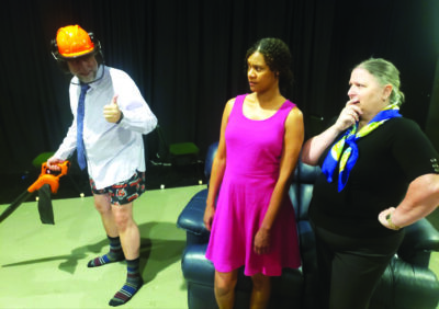 man with no pants wearing hardhat beside woman in pink dress and woman wearing black