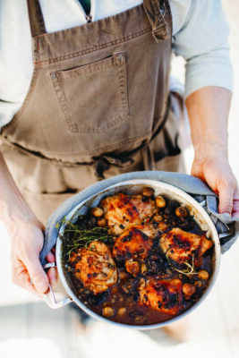 torso of man in brown apron holding pot of cooked chicken