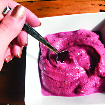 hand dipping spoon into white bowl filled with pink smoothie