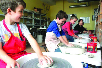 Line of children sitting at pottery wheels, in pottery studio, shaping clay
