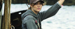 movie still, young woman in baseball cap, hoodie, and rubber overalls, sitting on fishing boat