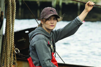 movie still, young woman in baseball cap, hoodie, and rubber overalls, sitting on fishing boat