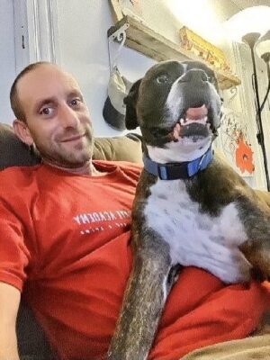 man sitting back on couch, smiling at camera, with dog in his lap
