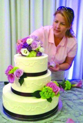 woman adding flower decorations to 3 tiered white frosted cake