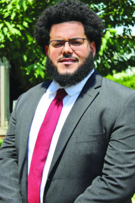 portrait of young man with afro and beard, wearing suit and glasses, standing outside