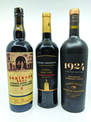 3 dark bottles of wine, with black and gold labels, on gray background