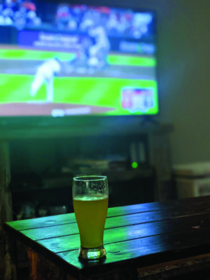 glass of beer on counter in front of TV showing baseball game