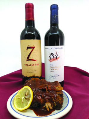 2 bottles on wine on red tablecloth next to plate of ribs