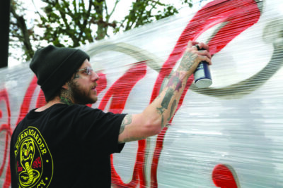 man spray painting graffiti mural onto wall made of cellophane