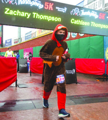 runner wearing turkey costume crossing the finish line of race on rainy day