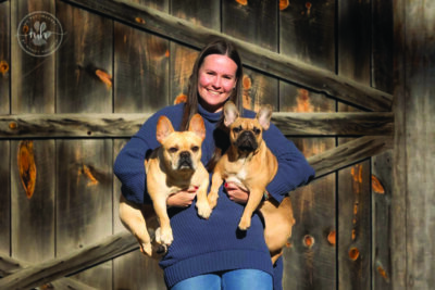 woman standing in front of wooden background holding two medium sized dogs