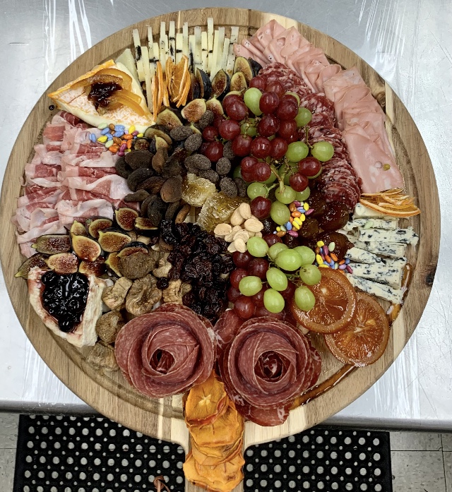 round wooden charcuterie board piles with deli meats, cheeses, dried fruits and grapes
