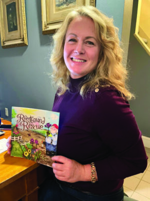 woman author at desk in house, holding her illustrated children's book and smiling
