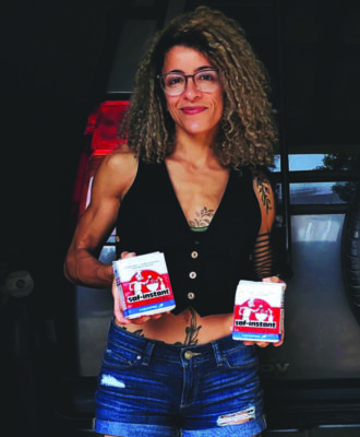 curly haired woman standing in front of car, holding boxes of baked goods