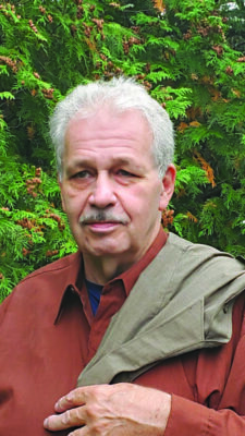 mature man posing in front of trees, jacket slung over shoulder
