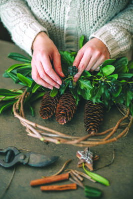 Woman working on christmas wreath with leaves and pine cones