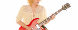 woman on white background, sitting cross legged while playing guitar