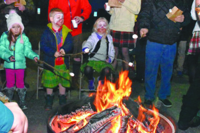 children wearing kilts holding sticks in front of bonfire at Hogmanay celebration