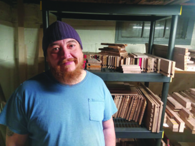 bearded man in t-shirt standing in front of shelves of wood for engraving