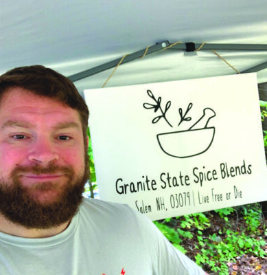 man with beard standing in front of sign that reads Granite State Spice Blends, outside
