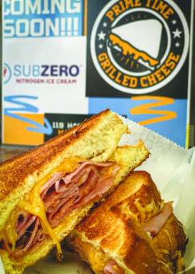 ham and grilled cheese sandwich in front of Prime Time Grilled Cheese restaurant sign