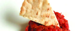 small bowl of tomato dip, triangular pita chip dipped in