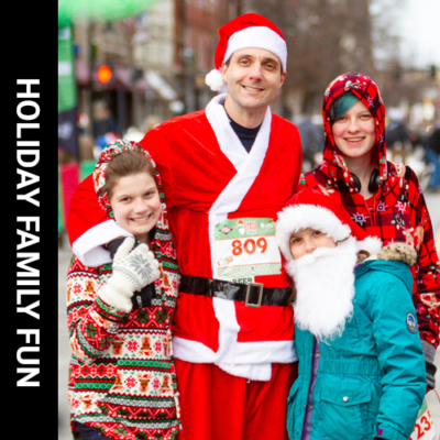 man wearing Santa costume standing with arms around a woman and 2 children, young boy wearing white beard