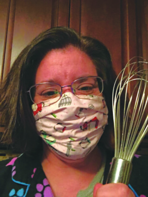 headshot of woman wearing facemask, holding whisk
