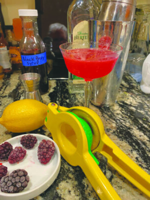 countertop with cocktail glass and ingredients, including lemon and frozen blackberries