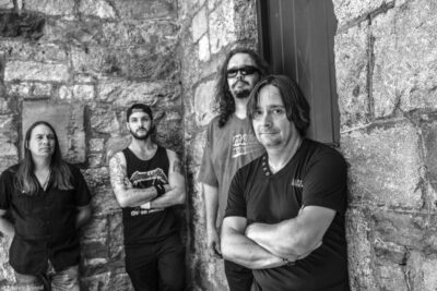 4 men posing against rough stone building, band members of Mindset X