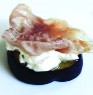 slice of plum topped with cream cheese and prosciutto
