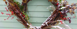 wreath made of dried plants hanging on side of house, dusted with snow