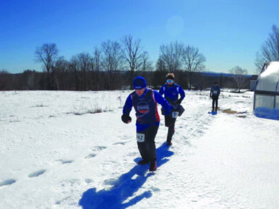 3 people running through a snowy field in racing gear