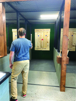 man at indoor ax throwing venue, holding ax, preparing to throw at target