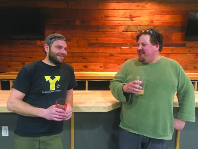 Two men steanding beside wooden table holding glasses of beer
