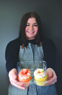 young woman in apron holding out two cupcakes in plastic takeout container