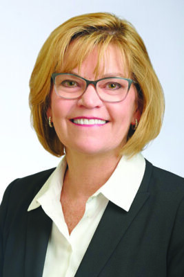 studio portrait of middle aged woman in business attire, wearing glasses, smiling