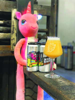 stuffed unicorn toy sitting with two cans of beer and a stemmed glass of beer
