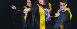 3 actors dressed in Hogwarts robes, pointing wands on dark stage