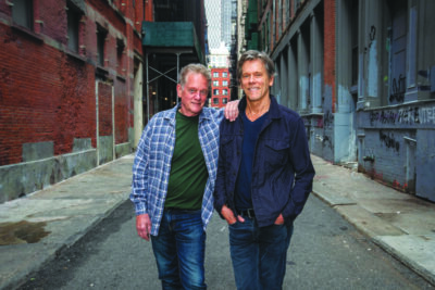 Micheal and Kevin Bacon of the band Bacon Brothers, posing in empty street, smiling
