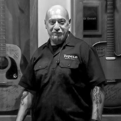 man wearing Tupelo employee shirt standing in front of guitars