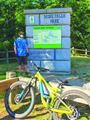 Cyclist standing in front of stone pillar with map of Mine Falls Park in Nashua, NH