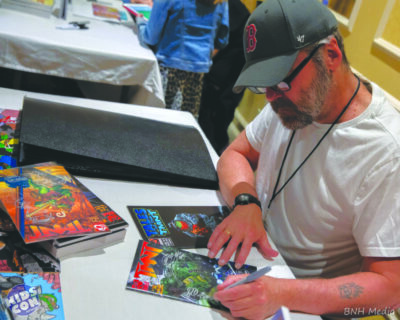 comic book artist signing copies of comics at convention table