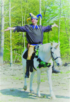 man dressed in jester hat, riding pony with horn on its head