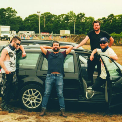 4 band members posing around an SUV