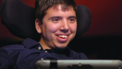 headshot of young man with cerebral palsy, in motorized chair, smiling