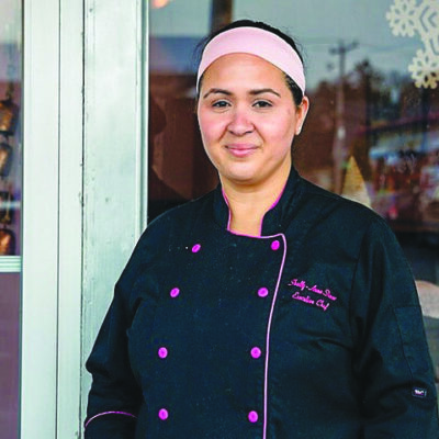 woman in chef's coat, standing in front of storefront window